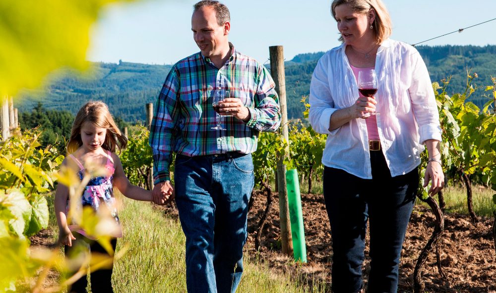 Mother, father, and daughter walking through the vineyard