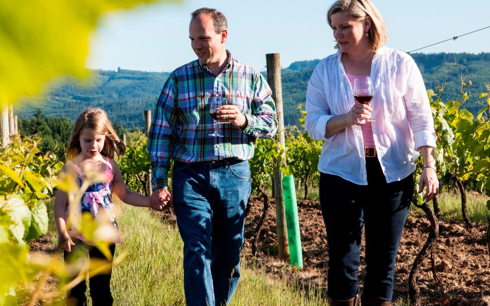 Mother, father, and daughter walking through the vineyard